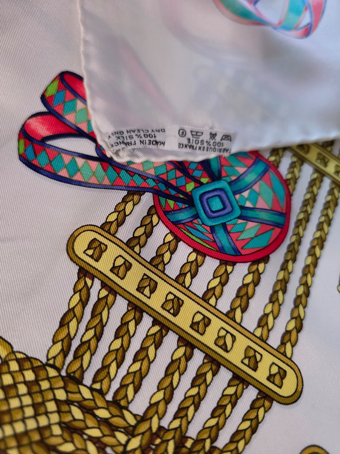 Hermès beige silk scarf featuring equestrian ribbon pattern and hand-rolled edges.