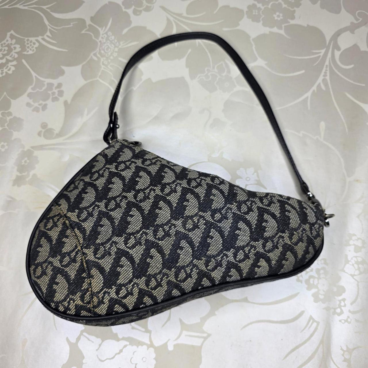 Dior messenger bag in grey, blue, and black with silver accents and saddle shape.